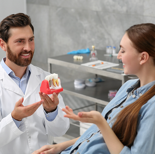 Male dentist showing female patient model of dental implant