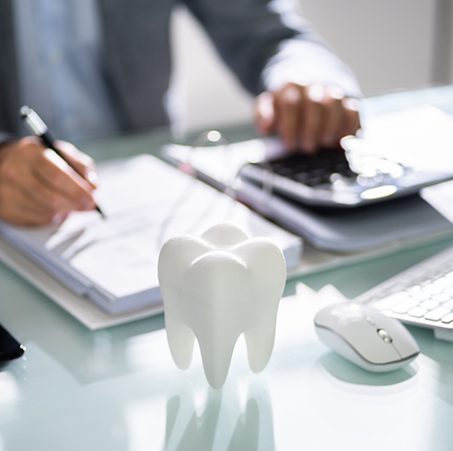 Model of tooth in foreground with someone filling out forms and using calculator in background