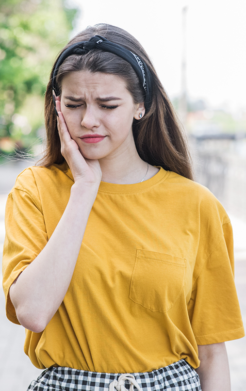 Woman in yellow shirt rubbing jaw in pain