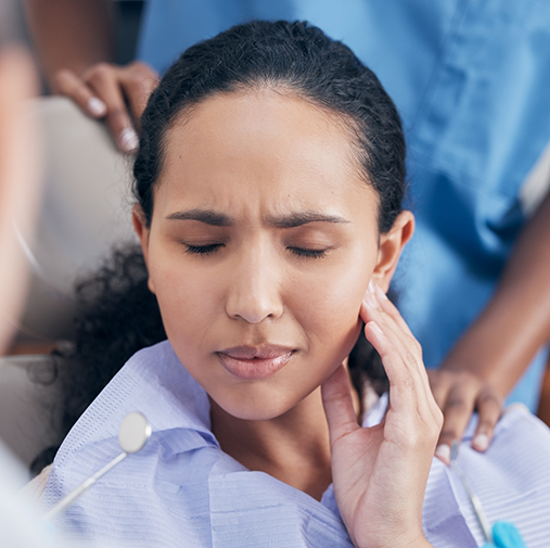 Woman in dental chair rubbing jaw in pain